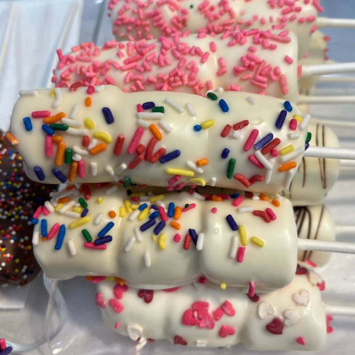 Stacked white chocolate Passover marshmallow sticks decorated with rainbow sprinkles and pink heart candies for festive treats.
