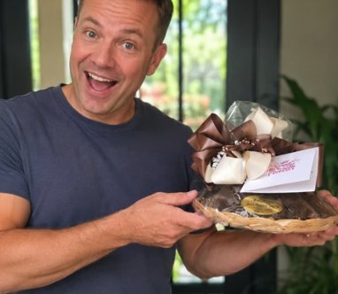 Smiling man holding a chocolate gift basket with brown and white bows from The Sweet Tooth