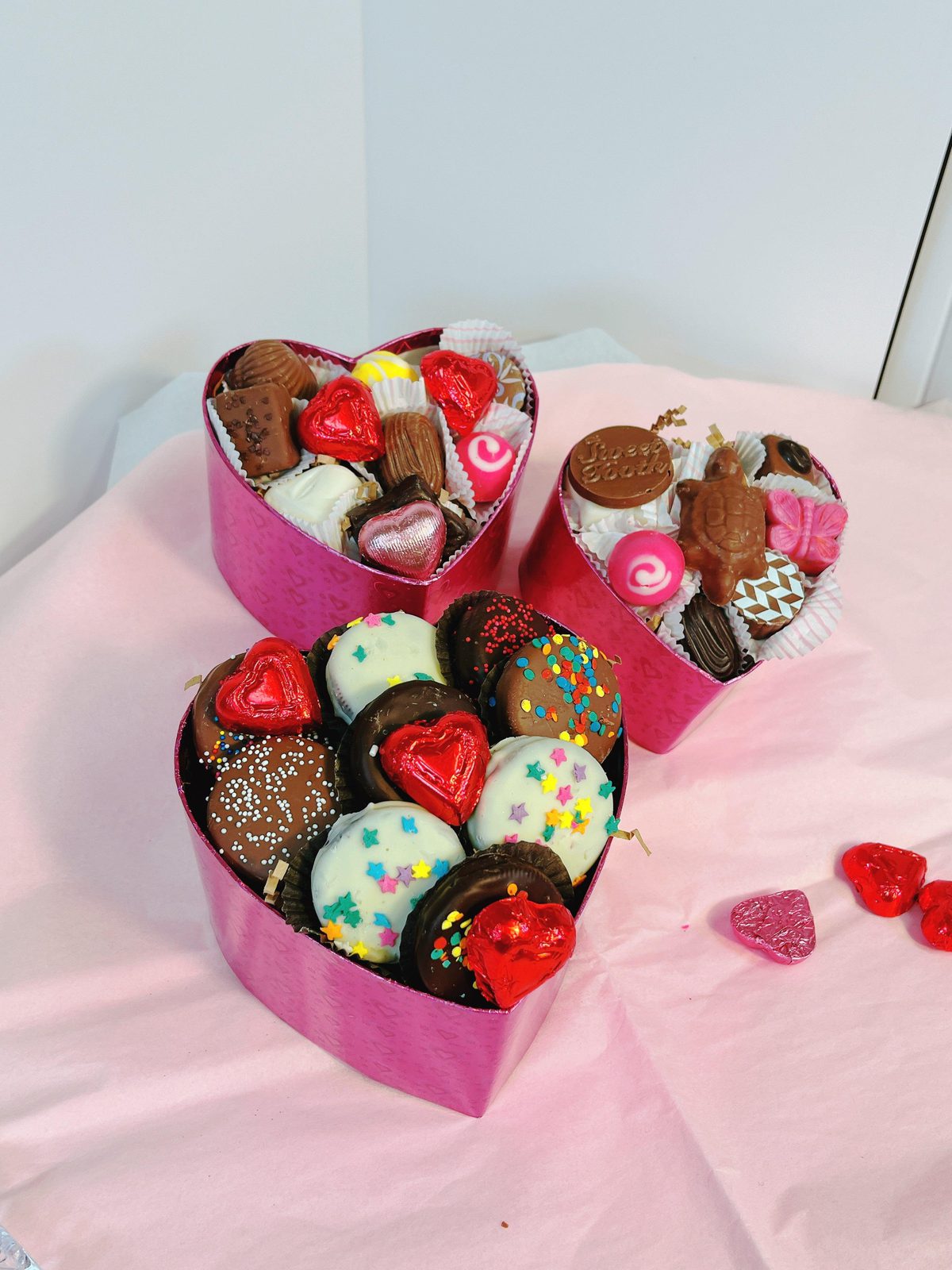 3-tier heart-shaped gift boxes filled with assorted chocolates and truffles in vibrant pink packaging, perfect for romantic gifting.