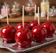 Glossy red candy apples on sticks with a 'Sweet Tooth' tray in the foreground.