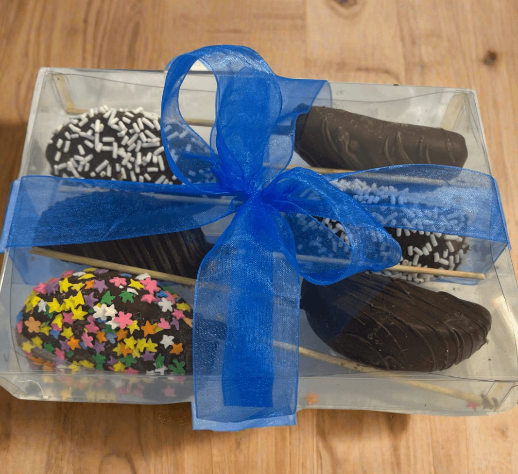 Chocolate Dipped  Apple Sticks 6-pack in clear gift box with blue ribbon, featuring assorted toppings like sprinkles and chocolate drizzle.