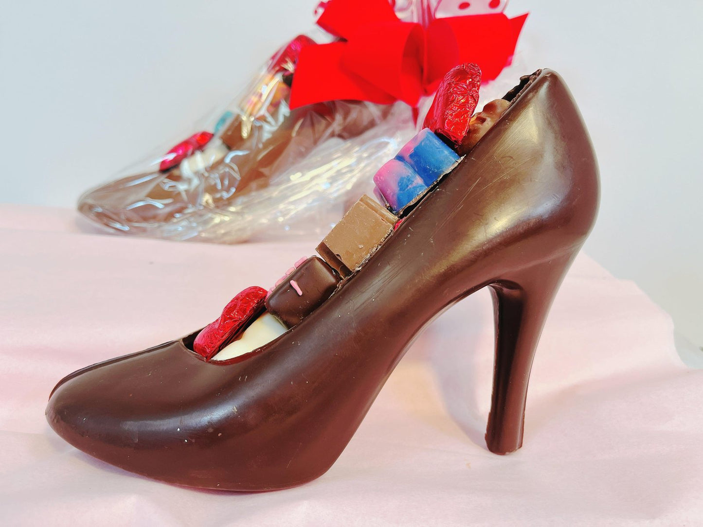 Chocolate high heel filled with assorted truffles and chocolates, displayed on pink fabric for gifting or special occasions.