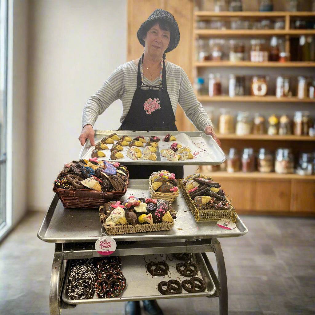 Assorted chocolate-dipped Hamantaschen cookies displayed on trays in a bakery setting, perfect for Purim celebrations and festive gifting.