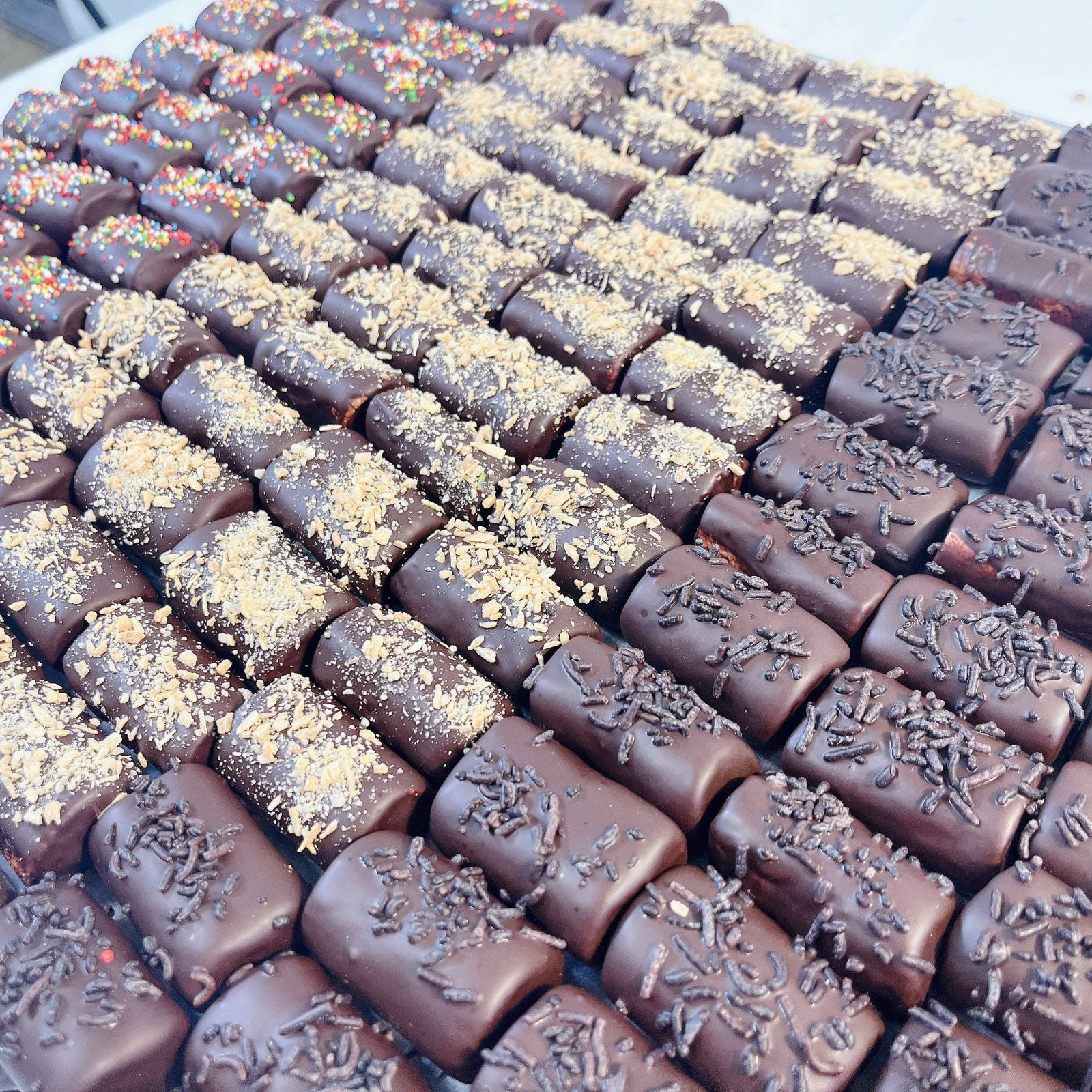 Rows of chocolate-covered logs with sprinkles from SUPREME - Passover, perfect for festive food gift assortments.