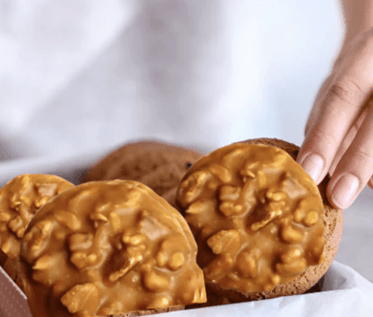 Hand selecting a Passover pecan praline from a gift box, showcasing vegan chocolate treats perfect for Passover 2025 by The Sweet Tooth.
