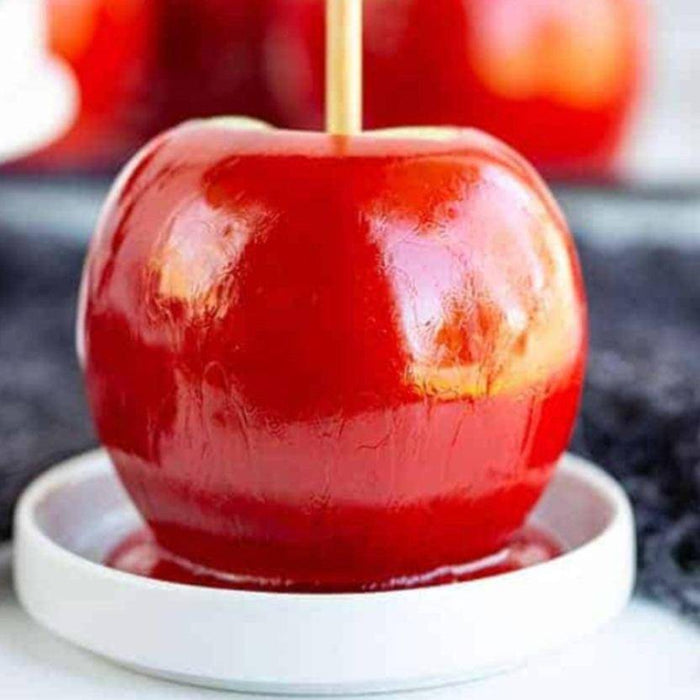 Glossy Classic Red Candy Apple on a white dish, featuring crisp apple dipped in vibrant red candy shell for a nostalgic snack.