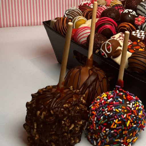 Assorted caramel apples with dark chocolate coating, nuts, and colorful sprinkles displayed in a tray for gourmet snack cake selection.