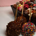 Assorted caramel apples with dark chocolate coating, nuts, and colorful sprinkles displayed in a tray for gourmet snack cake selection.