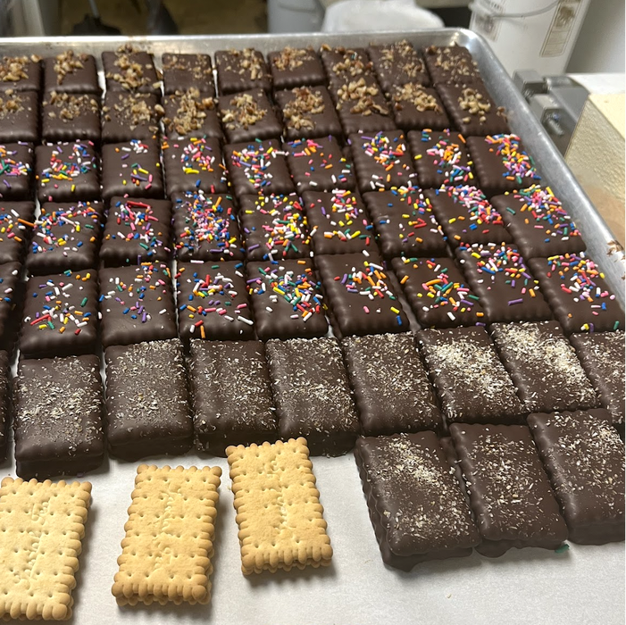 Tray of chocolate-covered cookies with various toppings on a metal surface.