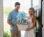 Man and woman holding a baby gift basket with a blue bow outdoors.