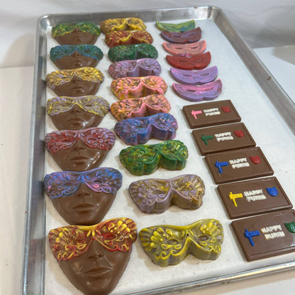 Tray of colorful hand-painted Chocolate Purim Masks and themed chocolate bars with 'Happy Purim' text, ideal for festive candy assortments.
