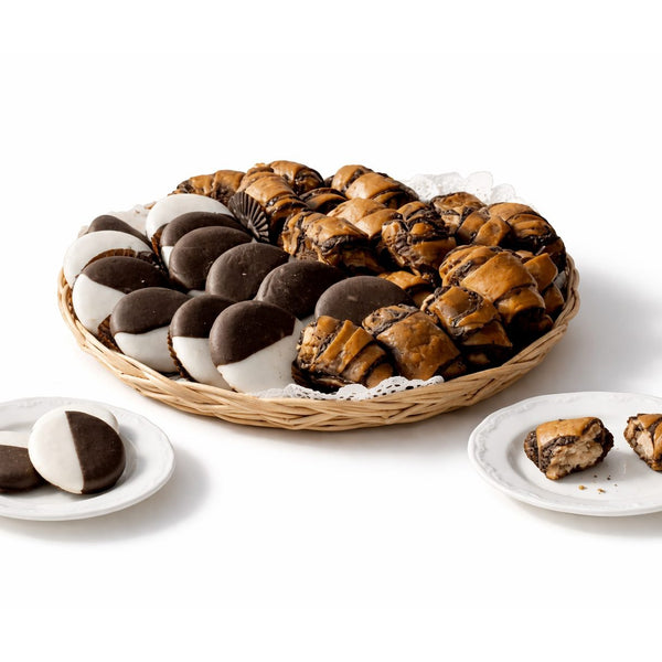 A wicker basket filled with Sonnny's famous black & white cookies with chocolate rugelach, arranged on a clean white studio background. A mix of soft cookies and rich pastry pieces ready for gifting or sharing.